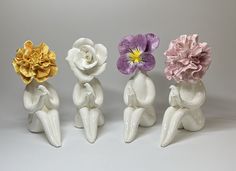 four ceramic figurines with flowers in the shape of people sitting on their knees