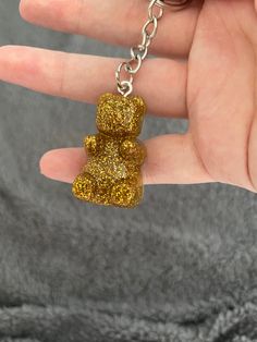 a hand holding a yellow teddy bear keychain in it's left hand