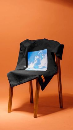 a black t - shirt sitting on top of a wooden chair in front of an orange wall