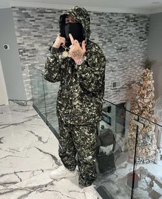 a man in camouflage is holding up his peace sign while standing next to a christmas tree