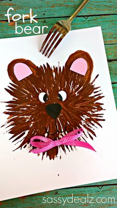 a brown bear with a pink bow on it's head is next to a fork