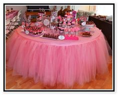 a table topped with lots of desserts on top of a hard wood floor covered in pink tulle