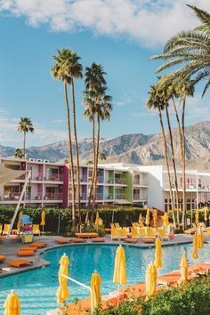 an outdoor swimming pool with yellow umbrellas and palm trees in front of the resort