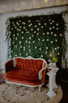 a red couch sitting on top of a rug next to a wall covered in flowers