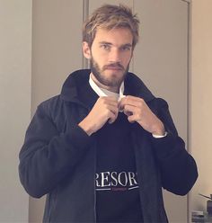 a man in a black jacket is tying his tie and looking at the camera while standing in front of a mirror