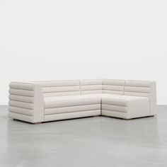 a white sectional couch sitting on top of a cement floor in front of a wall