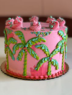 a pink and green cake with palm trees on it's top, sitting on a table