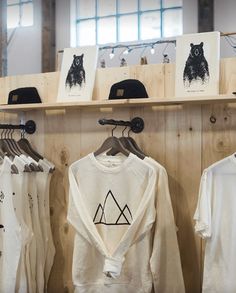 several t - shirts and hats are on display in a clothing store with wooden shelves