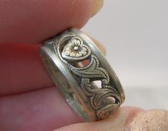 a close up of a person's hand holding a silver ring with an intricate design on it