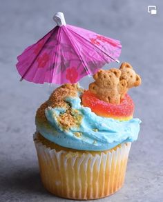 a cupcake with blue frosting and a teddy bear on top has an umbrella