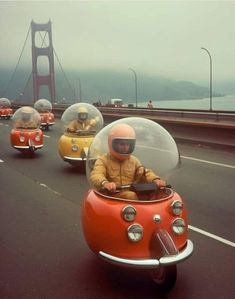 two people in small cars driving down the road with a bridge in the back ground