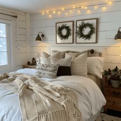 a bed with white sheets and pillows in a bedroom next to two christmas wreaths