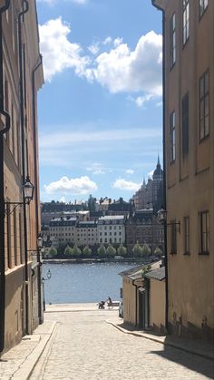 a cobblestone street with buildings on both sides and a body of water in the distance