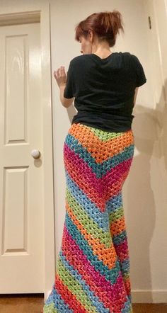 a woman standing in front of a door wearing a colorful crocheted skirt