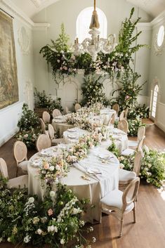 a dining room with tables and chairs covered in white linens, surrounded by greenery