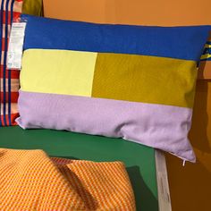 a colorful pillow sitting on top of a bed next to a yellow blanket and pillows