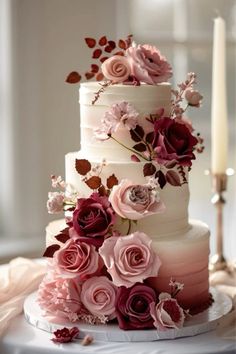 a three tiered cake with pink flowers on top and candles in the back ground