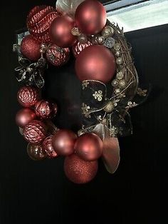 a wreath with red ornaments hanging from the side of a window sill in front of a black door