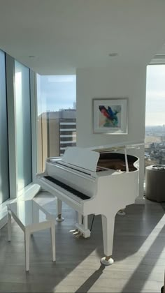 a white piano sitting in the middle of a living room next to a large window