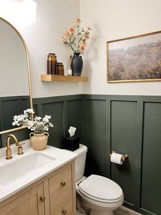 a white toilet sitting next to a sink in a bathroom under a framed painting on the wall