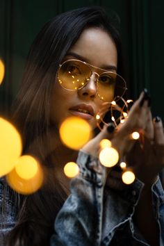 a woman wearing sunglasses and looking at her cell phone with lights in the back ground