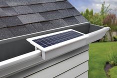 a solar panel mounted on the side of a house's gutter box in front of a green yard