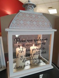 two lit candles in a white lantern with french writing on the front and back sides