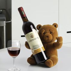 a brown teddy bear sitting next to a wine bottle and glass on a white table