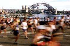 a group of people running down a street next to a bridge with a city in the background