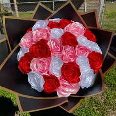 a bouquet of red, white and pink roses in a black paper box on grass