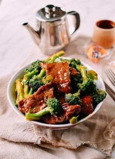 a white bowl filled with meat and broccoli on top of a table next to a teapot