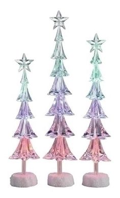 three small glass christmas trees on top of each other in pink and green colors with white base