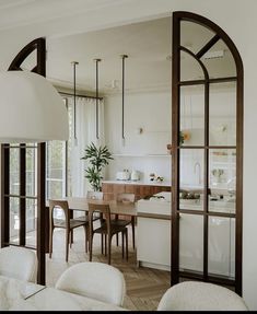 an open concept kitchen and dining room with white walls, wood flooring and large arched windows