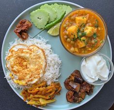 a white plate topped with rice, meat and veggies next to a bowl of sour cream