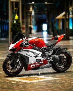 a red and white motorcycle parked on top of a brick floor next to a building