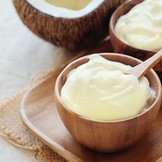 two coconuts with cream in them on a wooden tray