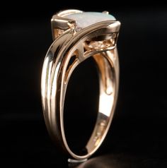 a gold ring with an opal stone in the center on a black background,