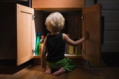 a little boy sitting on the floor in front of an open cabinet