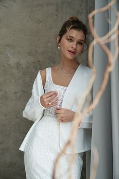 a woman in a white dress and jacket standing next to a curtain with her hands on her hips