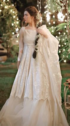 a woman in a wedding dress standing under a tree decorated with lights and garlands