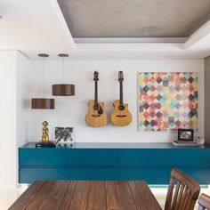 a room with guitars hanging on the wall and wooden table in front of blue cabinets