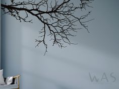 a tree branch with no leaves is hanging on the wall next to a chair and window