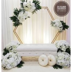 a white wedding set up with flowers and greenery in front of a gold hexagonal backdrop