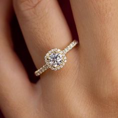 a woman's hand with a diamond engagement ring on her left hand and the center stone is surrounded by small round diamonds