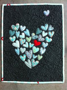 a quilted wall hanging with hearts and a red heart in the center on a black background