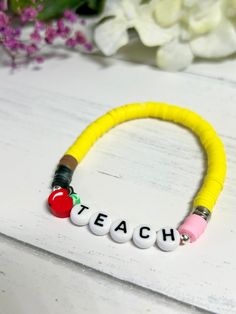 a yellow bracelet that says teach on it with two beads and an apple in the middle