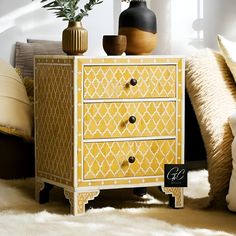 a yellow and white chest of drawers in a room with pillows, vases and plants