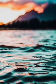 the sun is setting over water with mountains in the background