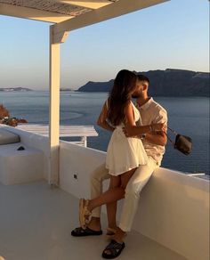 a man and woman kissing on a balcony overlooking the ocean