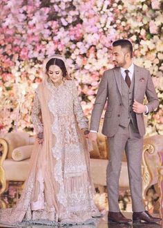 a man and woman standing next to each other in front of a floral wall holding hands